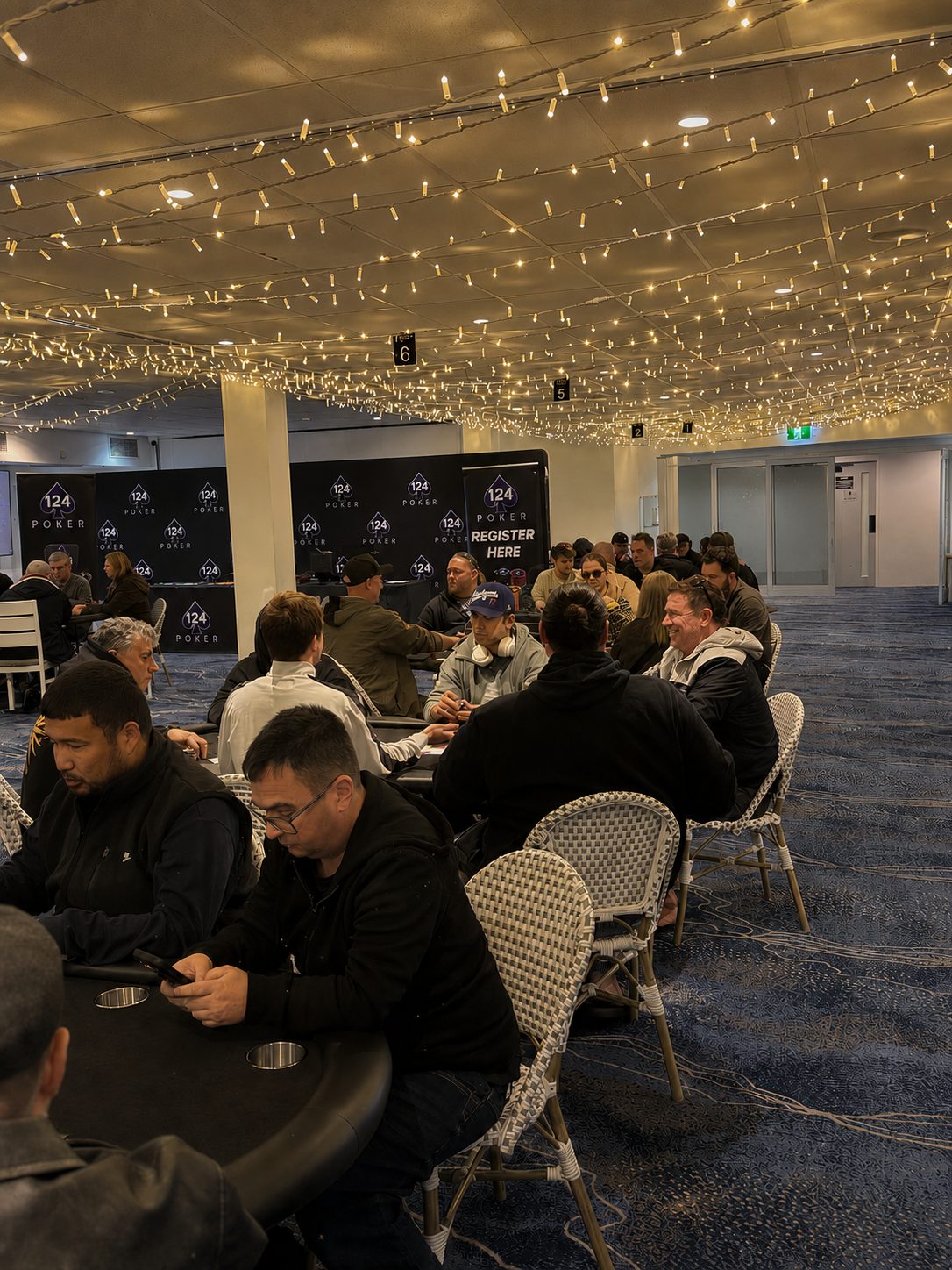 A 124 Poker weekly event under fairy lights, with full tables and a register here banner